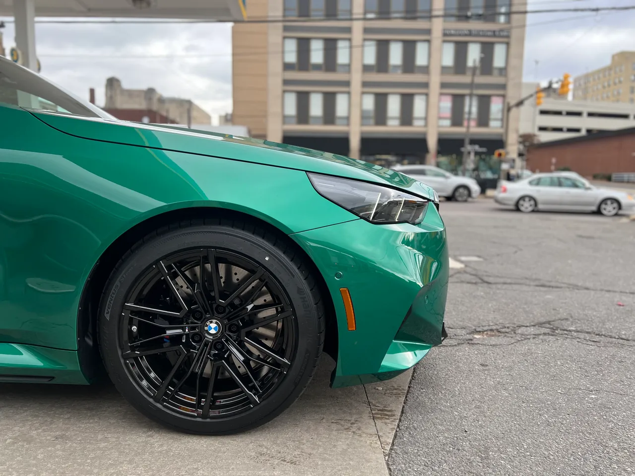 Green performance sedan parked on a downtown street, low front three-quarter angle