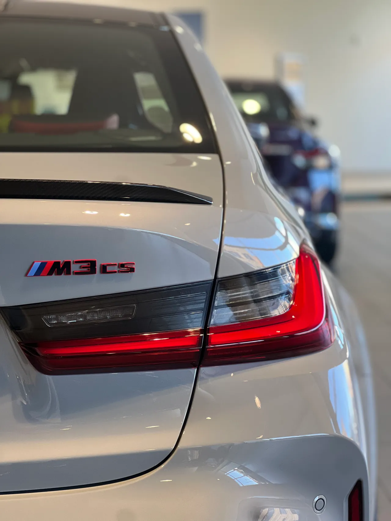 Rear badge and taillight of a silver sports sedan in a showroom