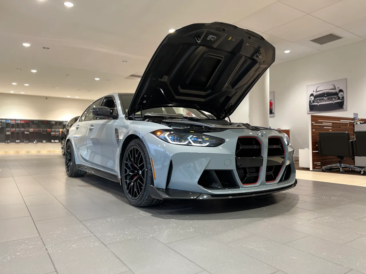Grey sports sedan with its hood raised on a bright showroom floor